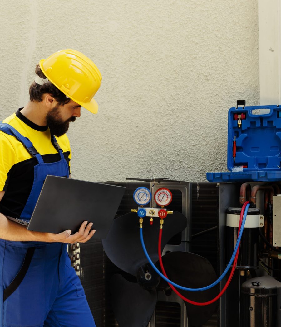 Trained engineer tasked with servicing outdoor air conditioner internal components, checking freon level and calibrating thermostats. Skilled technician looking over maintenance plan on laptop